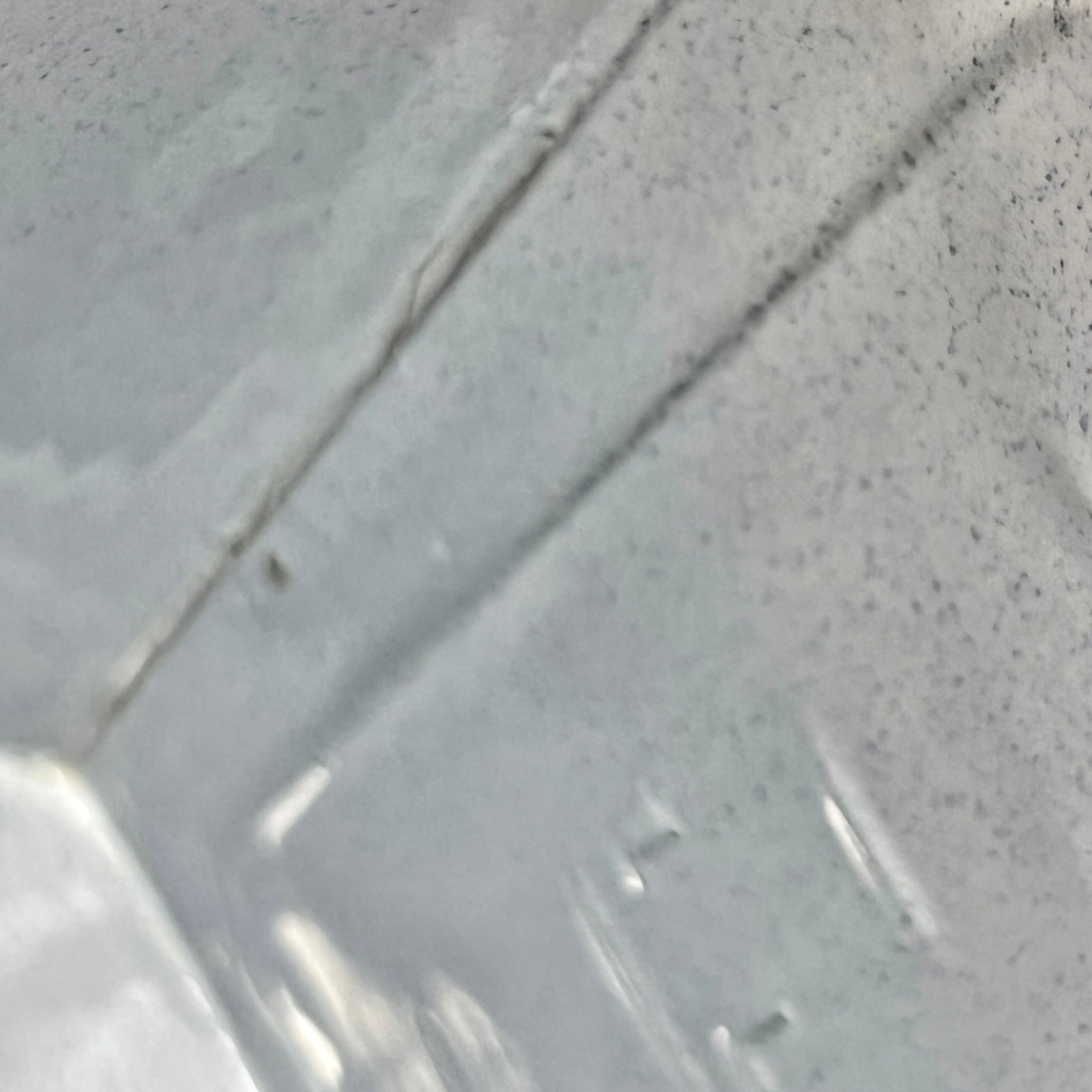 Close-up of the inside of an enamel planter with speckled glaze and blue rim on a white background