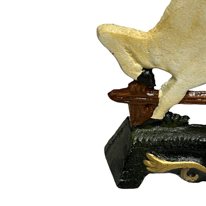 Close-up of a decorative figurine or sculpture showing part of a cream-colored animal body resting on a brown perch mounted to a black base with gold detailing, isolated on a white background.
