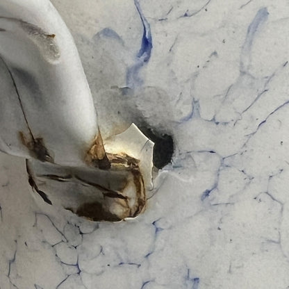 A close-up of a n enamel surface with a visible crack and dark discoloration near the centre, surrounded by faint blue veining.