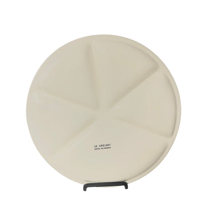 Round beige plate with a Le Creuset stamp on a white background