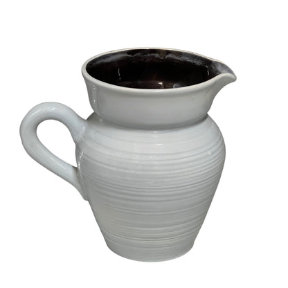 A white ceramic pitcher with a ribbed textured body, a curved handle, and a wide pouring spout, shown against a plain white background.