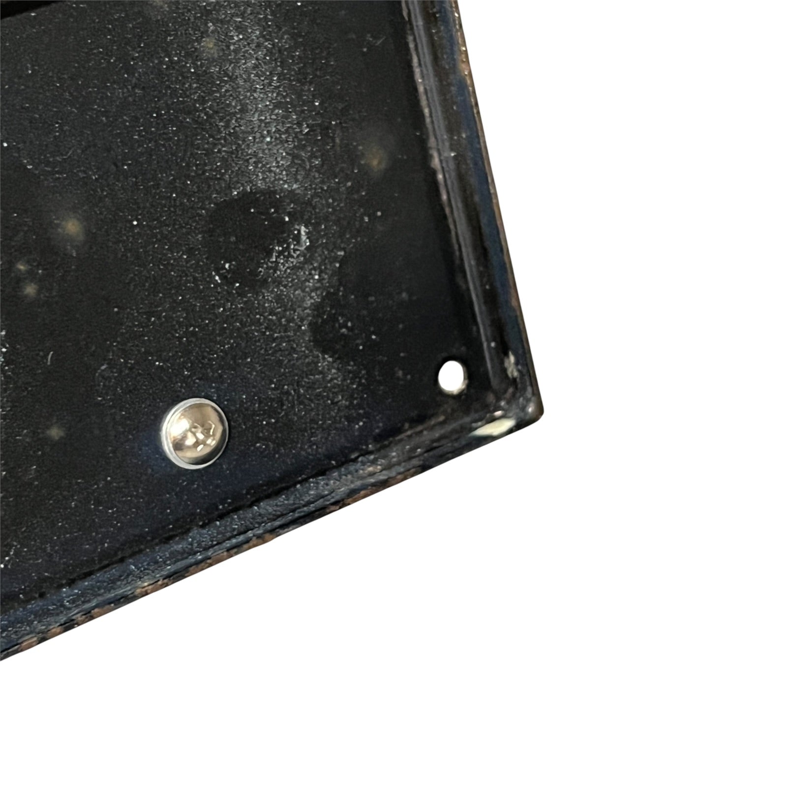 Close-up of the corner of a black metal mounting plate or bracket with a visible screw and mounting hole, shown against a plain white background.