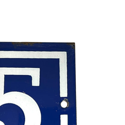 A close-up of a blue and white decorative sign showing part of a bold white geometric design and a small round mounting hole, photographed against a white background.