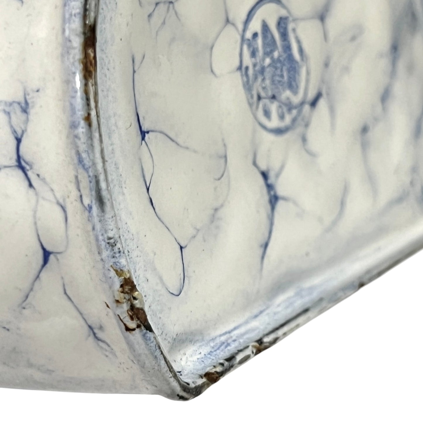 Close-up of a white enamel planter with blue floral underglaze patterns and visible wear along the rim.