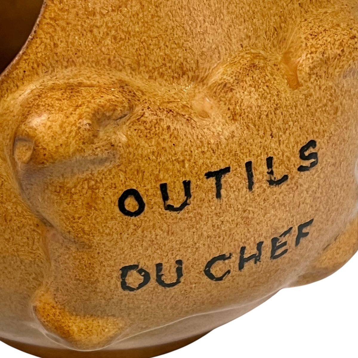 close up of a  French ceramic kitchen utensil holder with a honey-brown mottled glaze, rounded body and two large angled side openings. Raised front plaque inscribed Outils du Chef, meaning Chef's Tools. Traditional rustic French country kitchen pottery measuring 18.5 cm high, sourced from a French brocante and shown on a plain white background 
