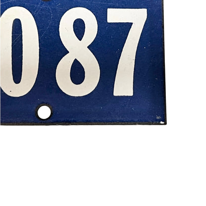 A close-up of a blue rectangular sign or plaque with large white numerals '2087' and a small round hole near the bottom left, shown against a white background.