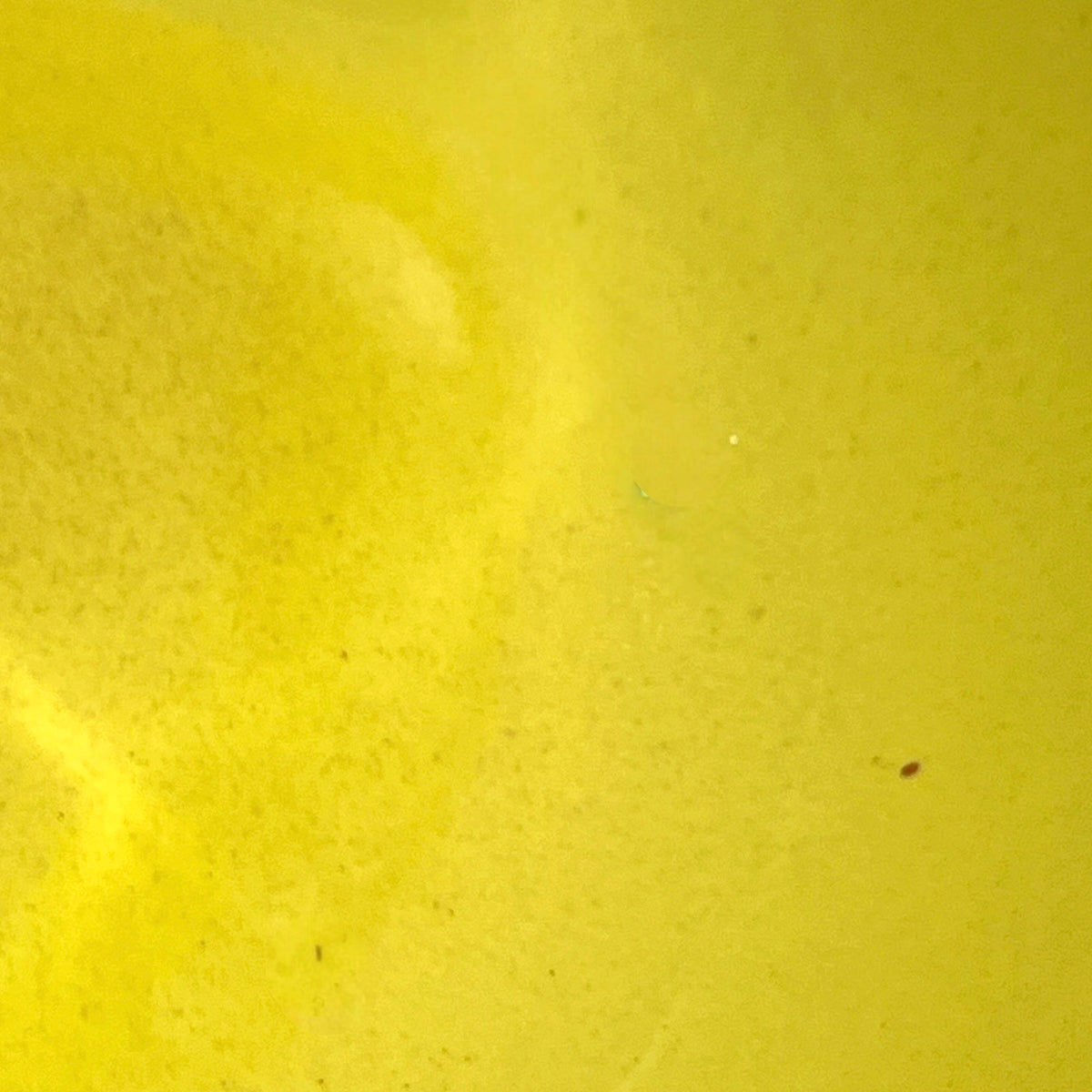 A close-up of a bright yellow textured surface with subtle tonal variation and tiny specks.