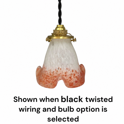 A hanging pendant light shade made of frosted white glass with orange speckling concentrated toward the bottom, attached to a black twisted cord and gold-toned metal fitting. Text below reads: 'Shown when black twisted wiring and bulb option is selected.
