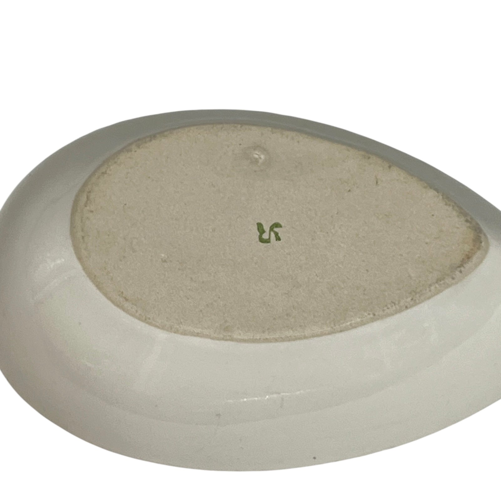 Close-up of the underside of a white ceramic dish or bowl, showing a textured beige center and a small green mark.