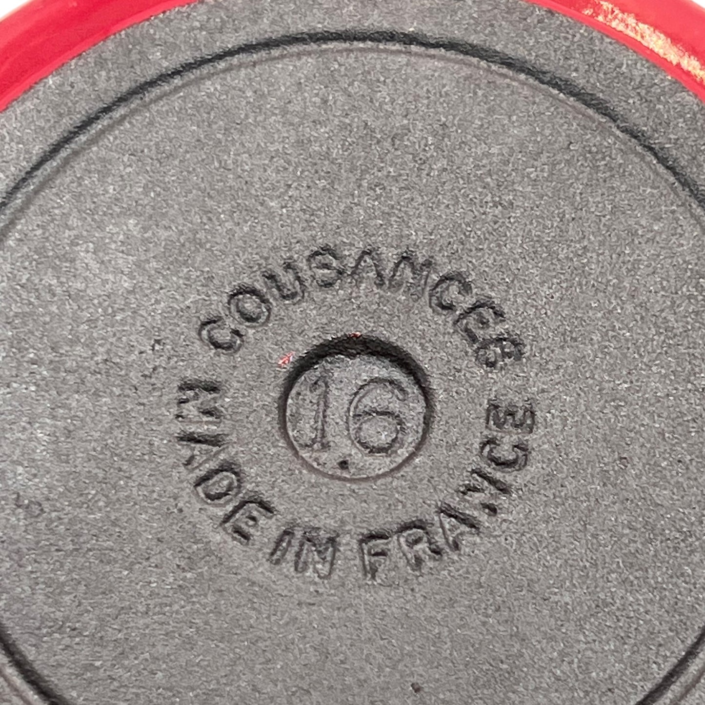 Close-up of the bottom of a dark gray cast iron weight plate, embossed with 'COUSANCES MADE IN FRANCE' and the number '16'.