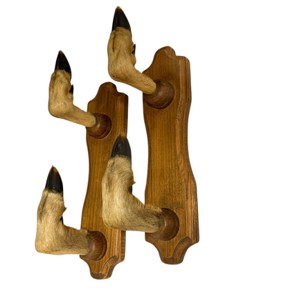 A pair of vintage-style wooden wall hooks shaped like animal hooves, featuring natural tan fur with black tips mounted on medium brown wood plaques, shown against a plain white background.