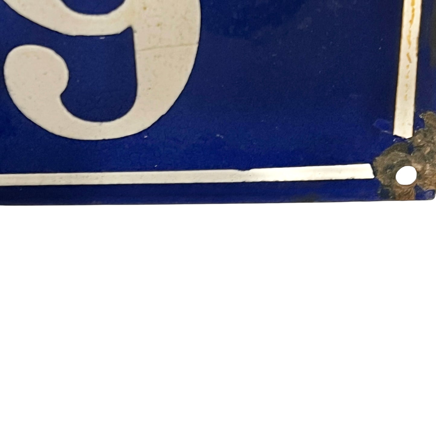 Close-up of a blue enamel sign with a white serif numeral and a weathered metal corner bracket holding it.