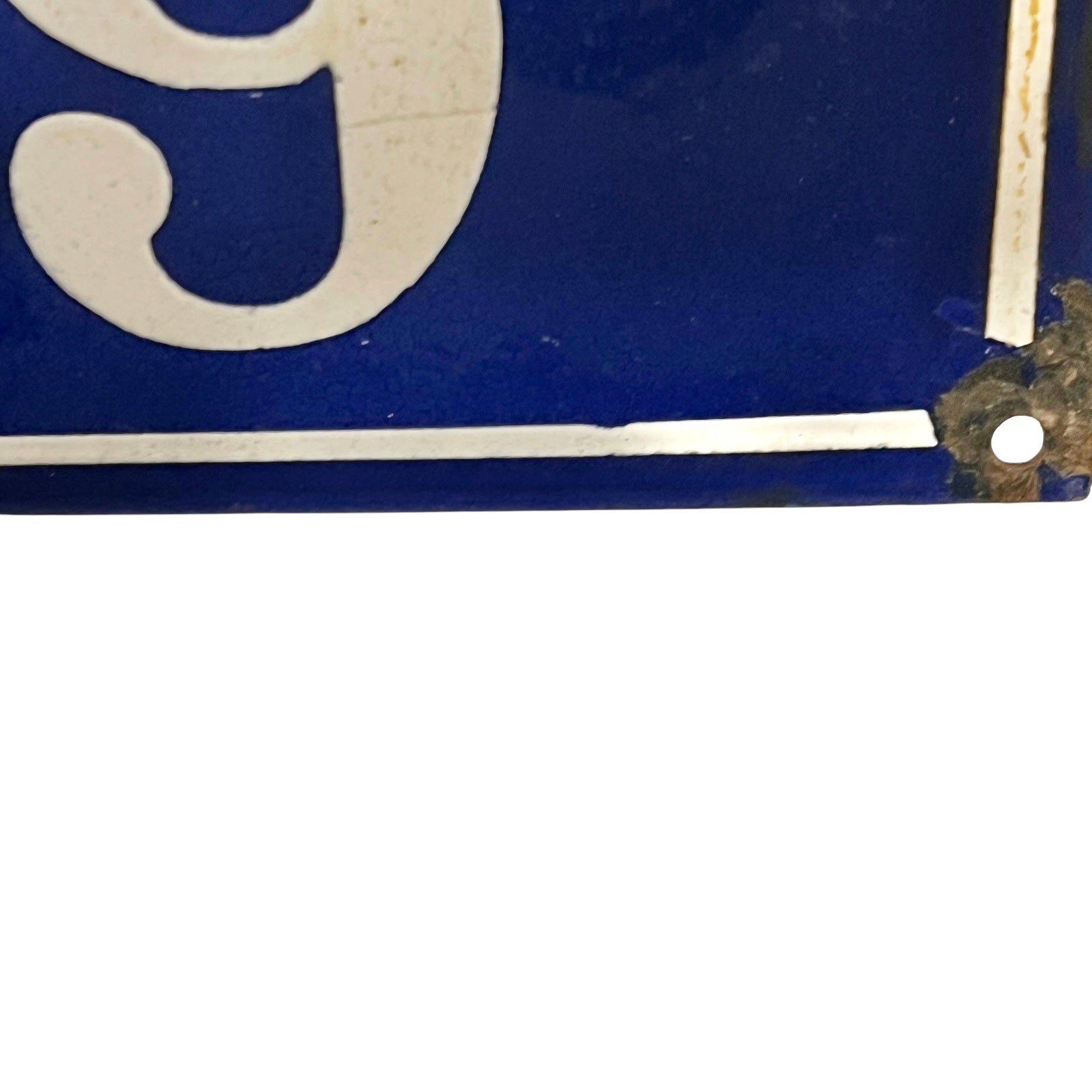 Close-up of a blue enamel sign with a white serif numeral and a weathered metal corner bracket holding it.