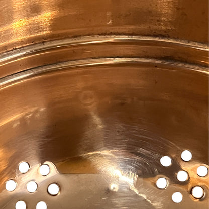 Copper colander with brass handles and feet on a white background
