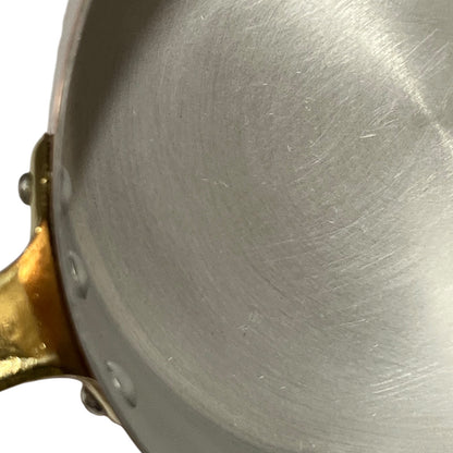 Close-up of the interior of a brushed aluminium lined saucepan or pan with a brass handle attachment visible on the left side.