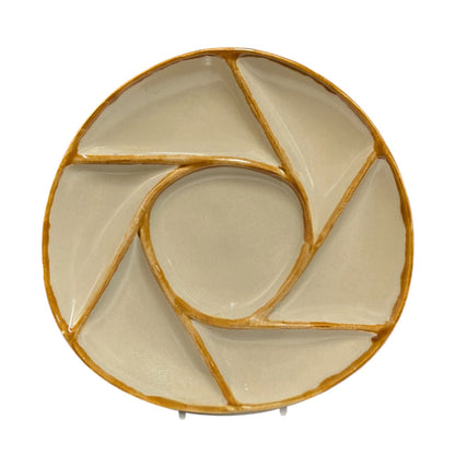 A round ceramic serving platter with a spiral segment design, featuring a glossy cream glaze and a rustic gold-brown rim, shown on a plain white background.
