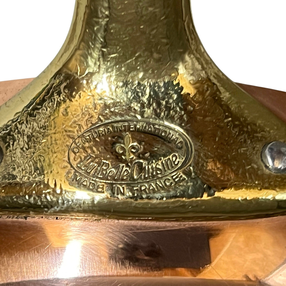 Close-up of a polished brass or bronze metal surface with an embossed oval logo reading 'Celtic International La Belle Cuisine Made in France' and a fleur-de-lis symbol.