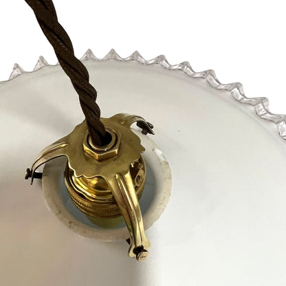 A close-up of a vintage brass ceiling light fixture socket with a dark brown twisted cord, set against a white glass shade.