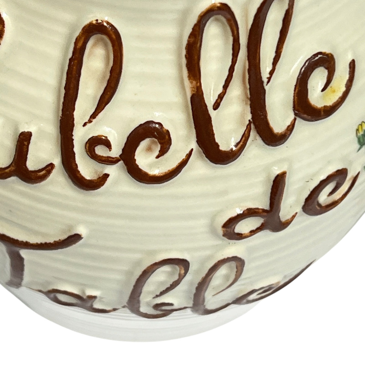 Close-up of a white ceramic table decor piece with raised brown cursive lettering and a ribbed surface.