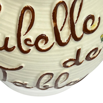 Close-up of a white ceramic table decor piece with raised brown cursive lettering and a ribbed surface.