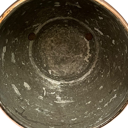 The interior of a dark gray cast iron pot or bucket, showing a distressed, weathered surface with white chipped paint and a copper-colored rim visible at the top.