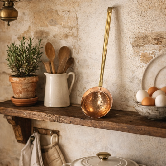 Kitchen shelf with copper slotted spoon, wooden spoons, and eggs against a stone wall.