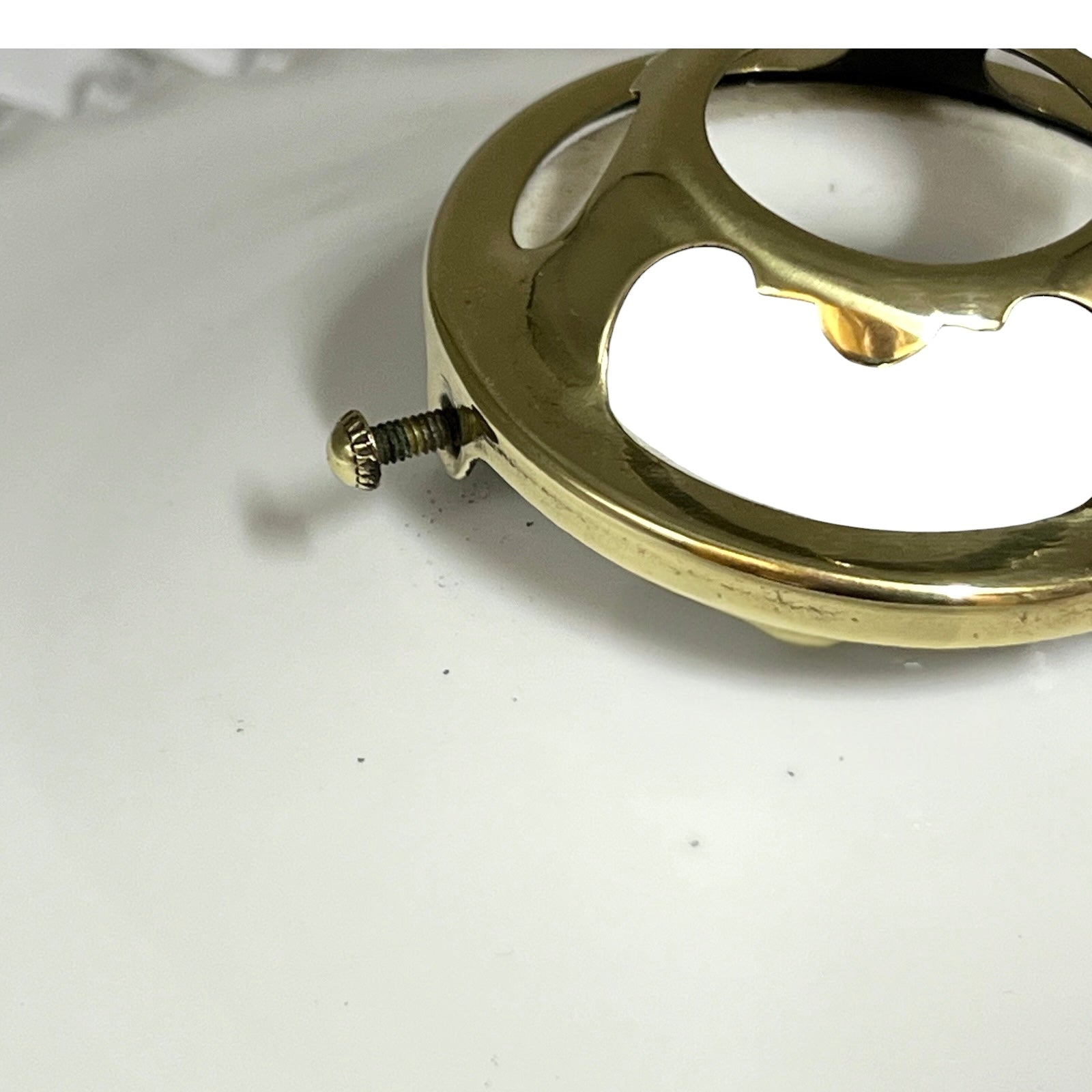 A close-up of a polished brass circular hardware piece with a protruding screw, resting on a plain white surface.