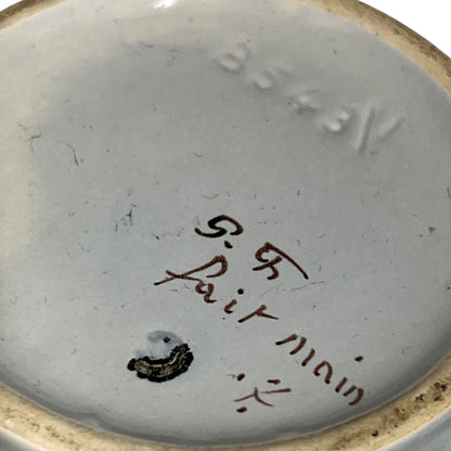 Close-up of the interior bottom of a ceramic dish or bowl, showing a light gray glazed surface with embossed numbering, a small dark stain, and handwritten markings reading 'R.R.