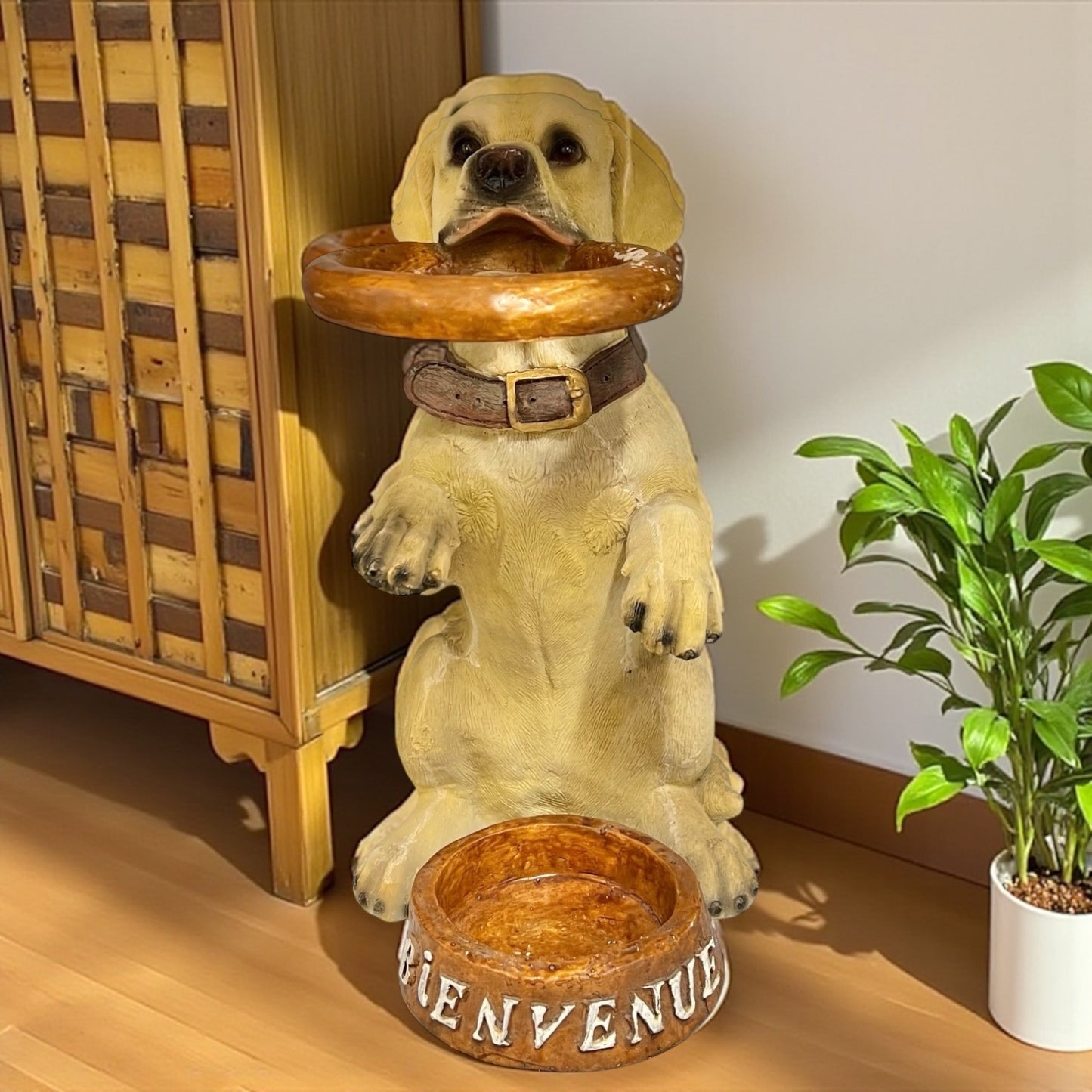 Dog umbrella stand with a  bowl on its head and 'BIENVENUE' bowl below, next to a plant and wooden cabinet for sale from All Things French Store.