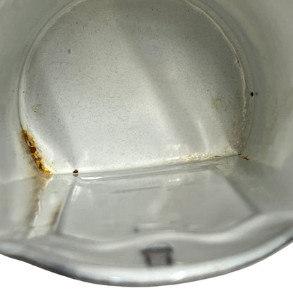 Close-up of the inside of a white enamel container or bucket, showing a stained and worn interior with rust-like discoloration near the bottom left corner.