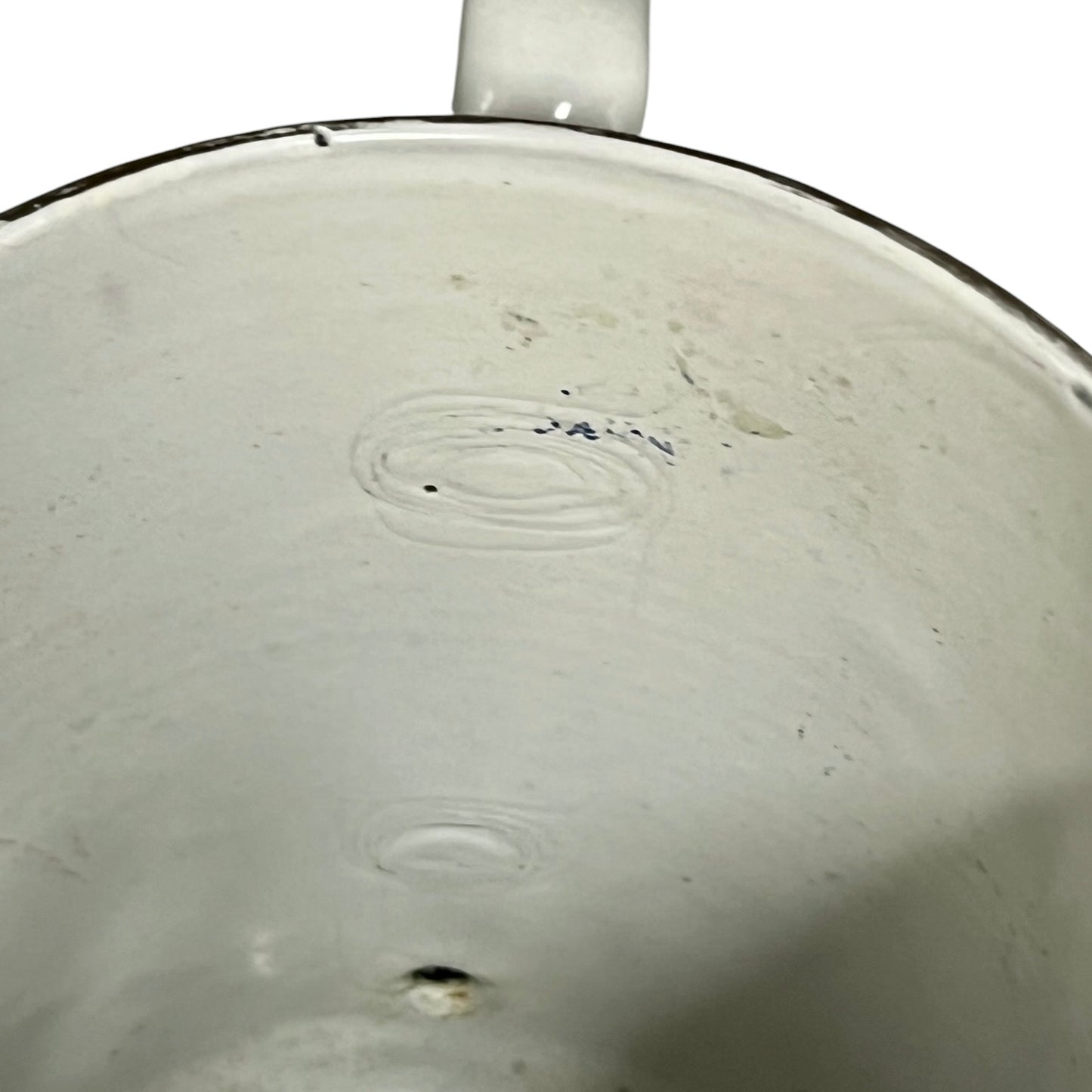 Close-up of the inside of a white enamel pot with a dark rim, showing some scuffs, stains, and ring marks on the surface.