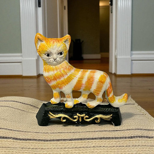 Cast iron cat doorstop with orange and white stripes on a decorative stand against a cosy lounge background