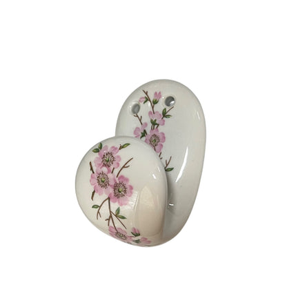 Two glossy white ceramic wall hooks decorated with pink cherry blossom flowers and green leaves, shown against a plain white background.
