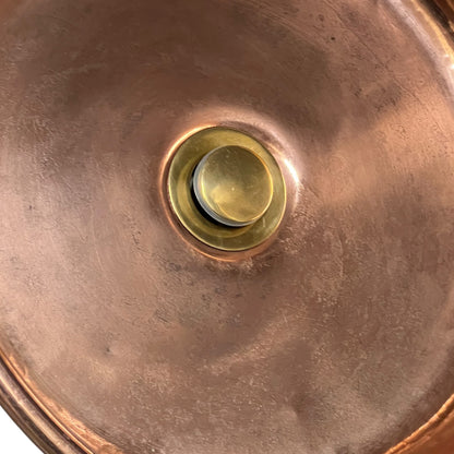 Close-up of the interior bottom of a copper basin, showing a warm metallic copper surface with a brass pop
up waste