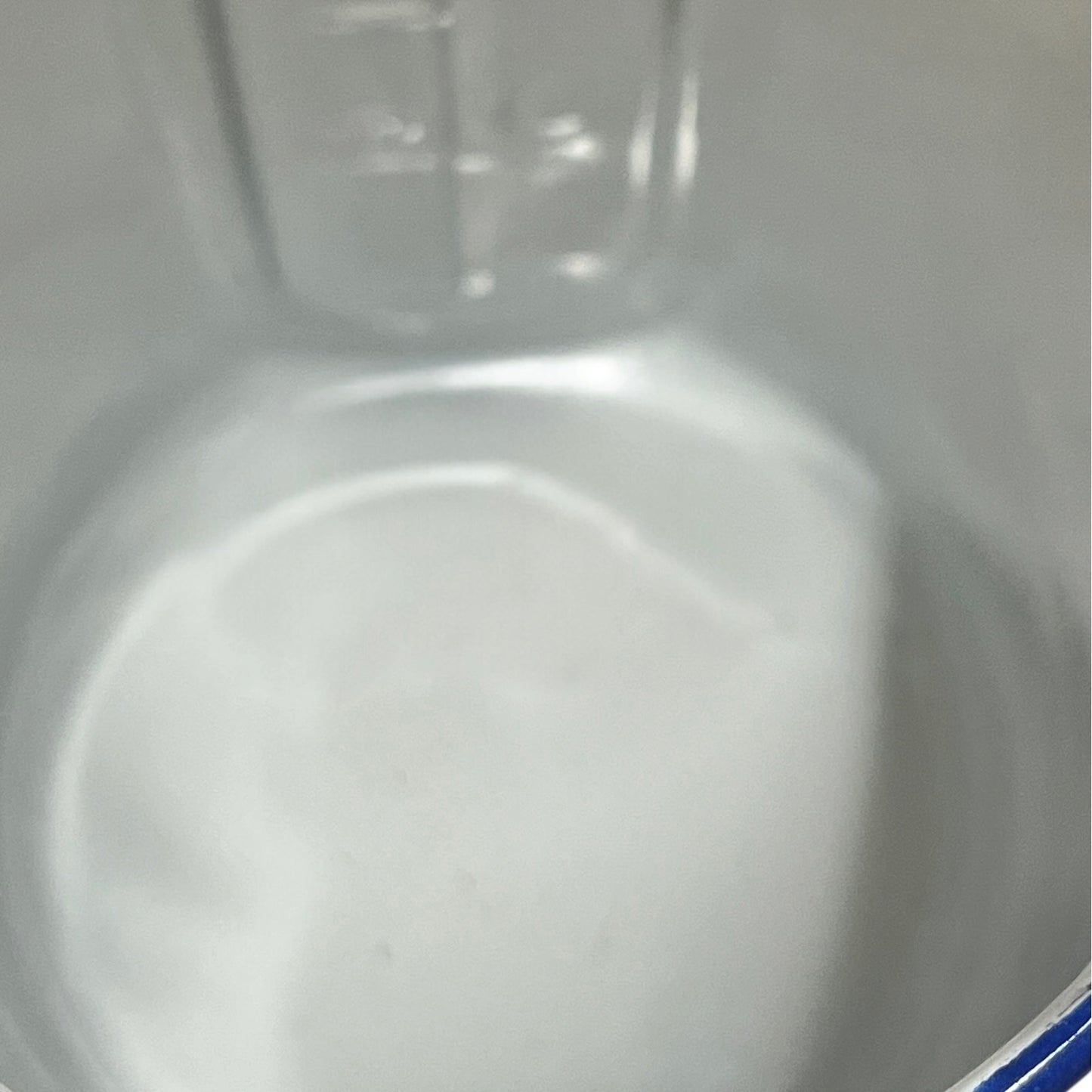 Close-up of the inside of a white enamel plant pot with a blue rim on a plain white background.