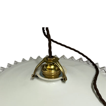 Close-up of a vintage pendant light fixture with a white glass shade, a brass metal canopy, and a dark brown hanging cord against a white background.