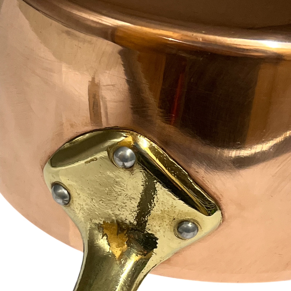 Close-up detail of a copper pot with a polished brass handle and rivets, showing the reflective metallic surfaces against a white background.