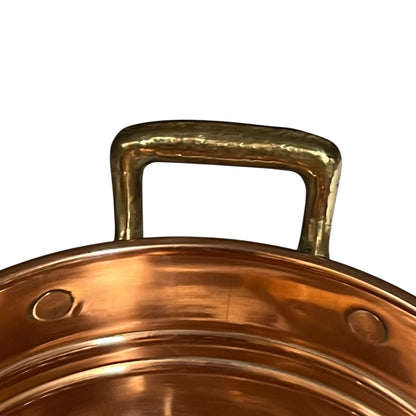 Close-up of a hammered brass pot handle attached to a copper-colored metal pot rim, shown against a plain white background.
