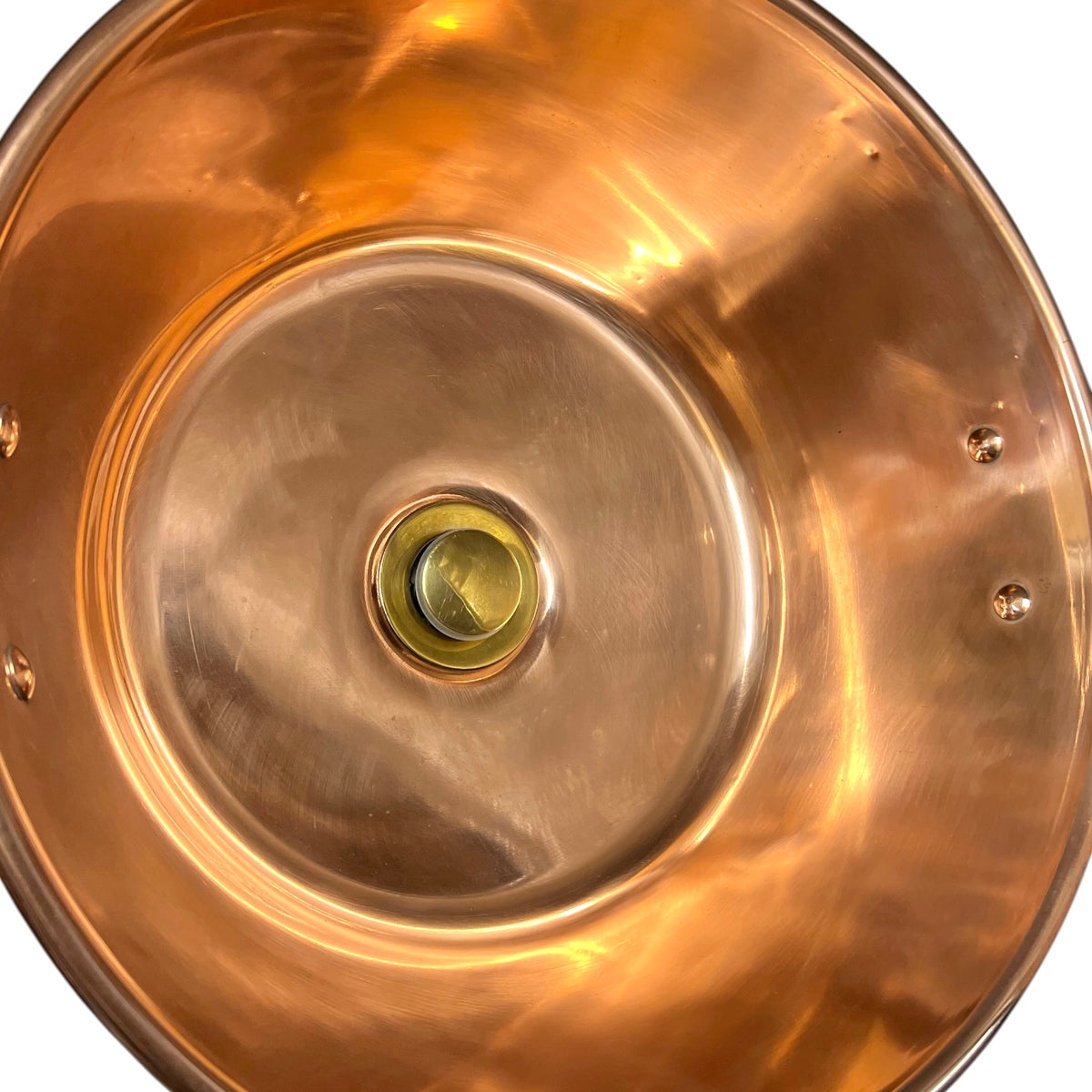Close-up of the interior of a polished copper or brass bowl, showing a warm metallic copper-gold finish with a small central hole and rivet details.