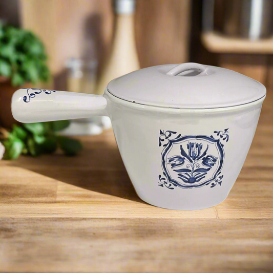 White enamelled cast iron pot with blue floral design and handle on a wooden table