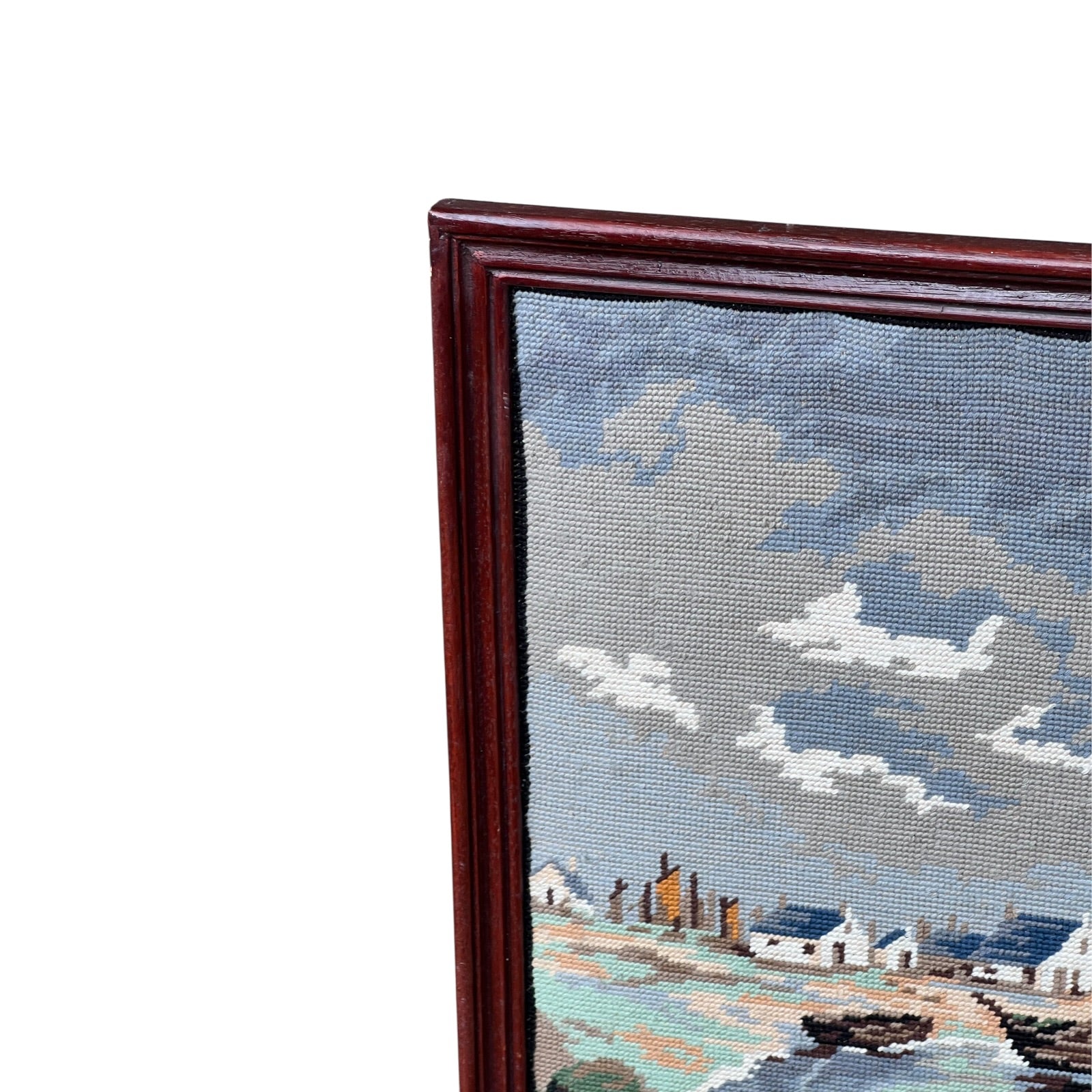 Close up of framed tapestry needlepoint with a coastal scene and wooden frame on a white background