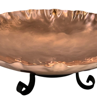Copper bowl with wavy edge and black metal stand on a white background