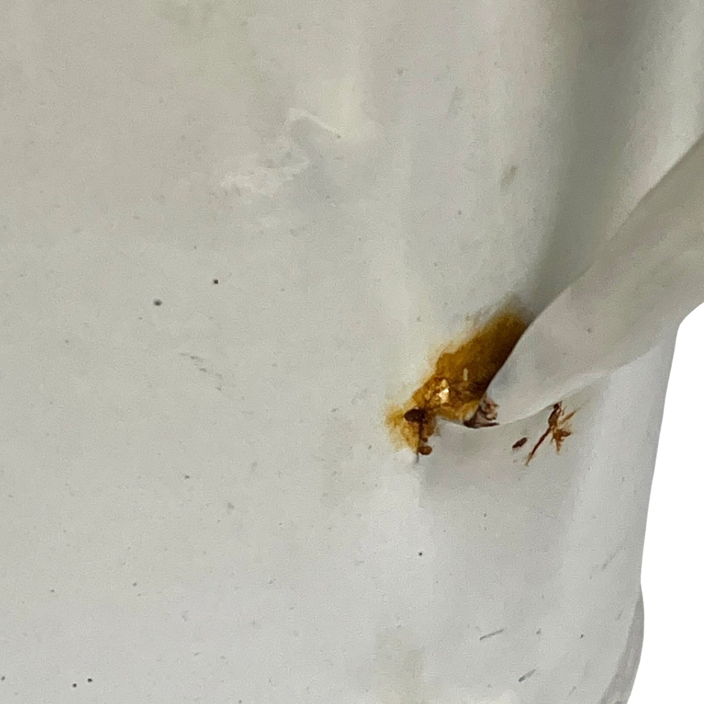 A close-up of a white enamel planter with a small amber-brown stain or residue near the rim, with a white utensil or straw-like object entering from the right side.