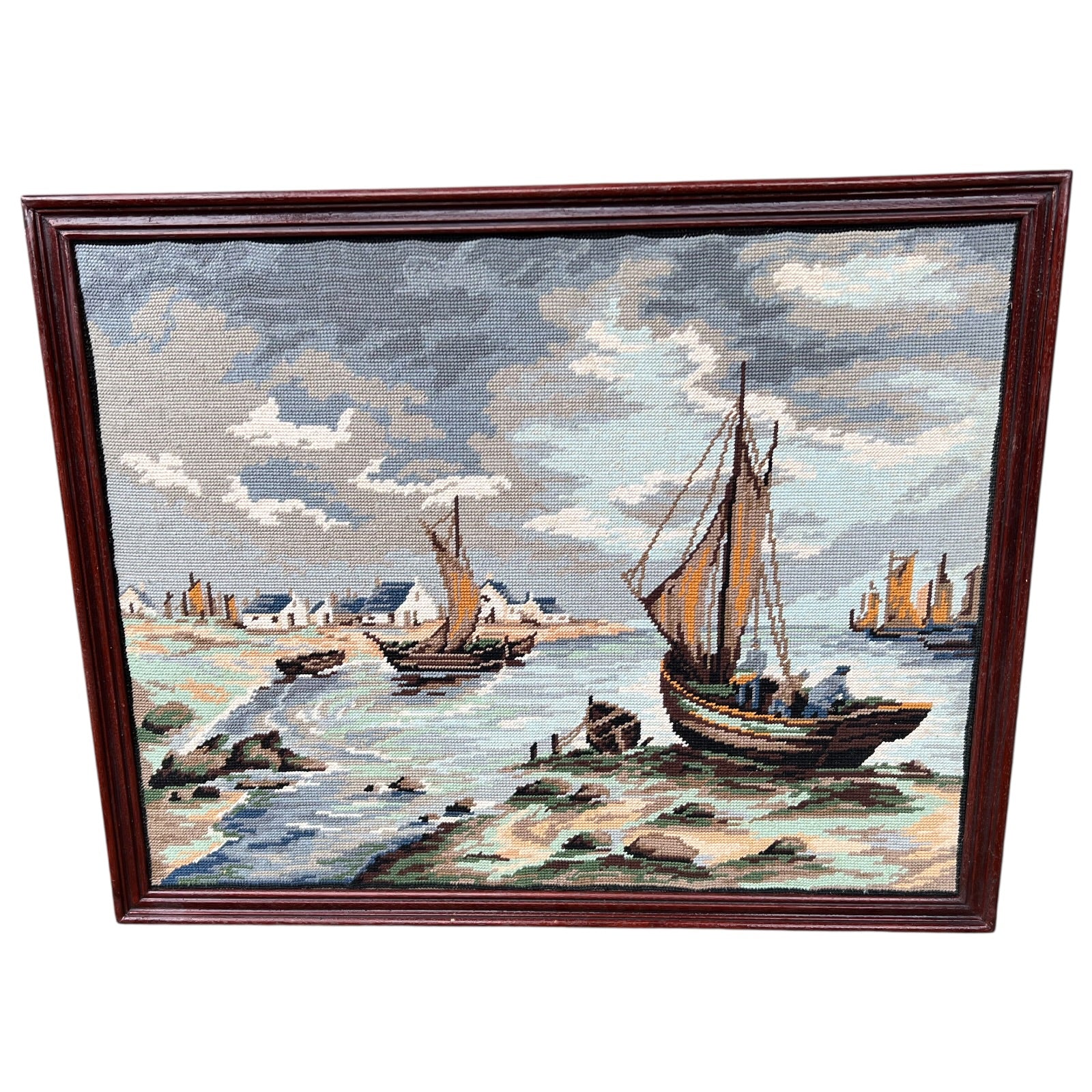 Framed needlepoint of a coastal scene with boats and houses on a white background.