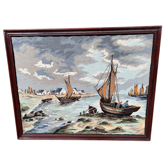 Framed needlepoint of a coastal scene with boats and houses on a white background.