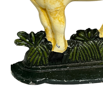 Close-up of a decorative figurine showing the lower legs of a pale yellow animal standing on a dark green leafy base against a white background.