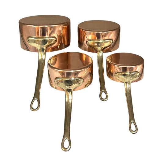 Set of four copper saucepans with brass handles on a white background