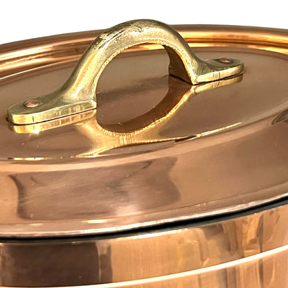 Close-up of a copper lid with a handle on a copper casserole pot