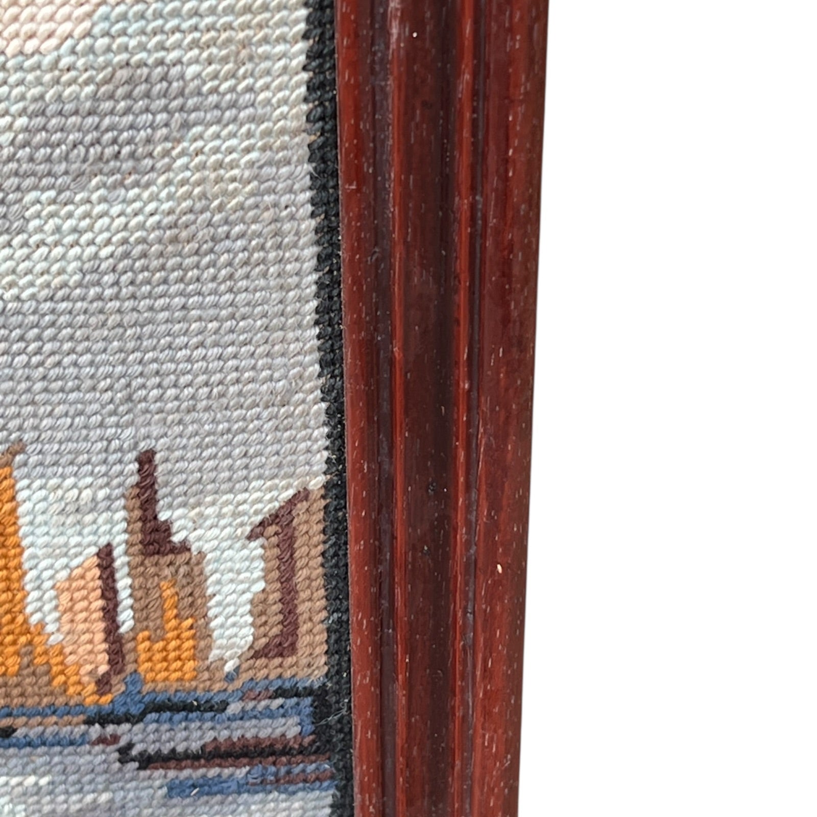 Close up of framed tapestry needlepoint with a coastal scene and wooden frame on a white background