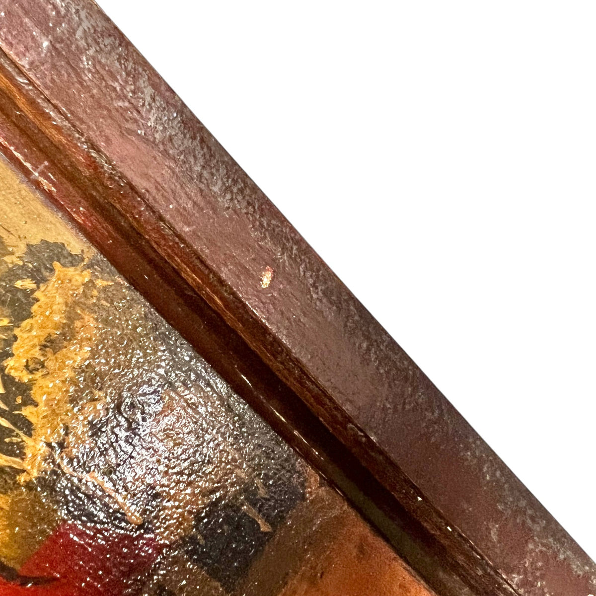 Close-up detail of a framed artwork corner, showing a dark reddish-brown wooden frame bordering a textured painting with gold, red, and dark tones against a white background.